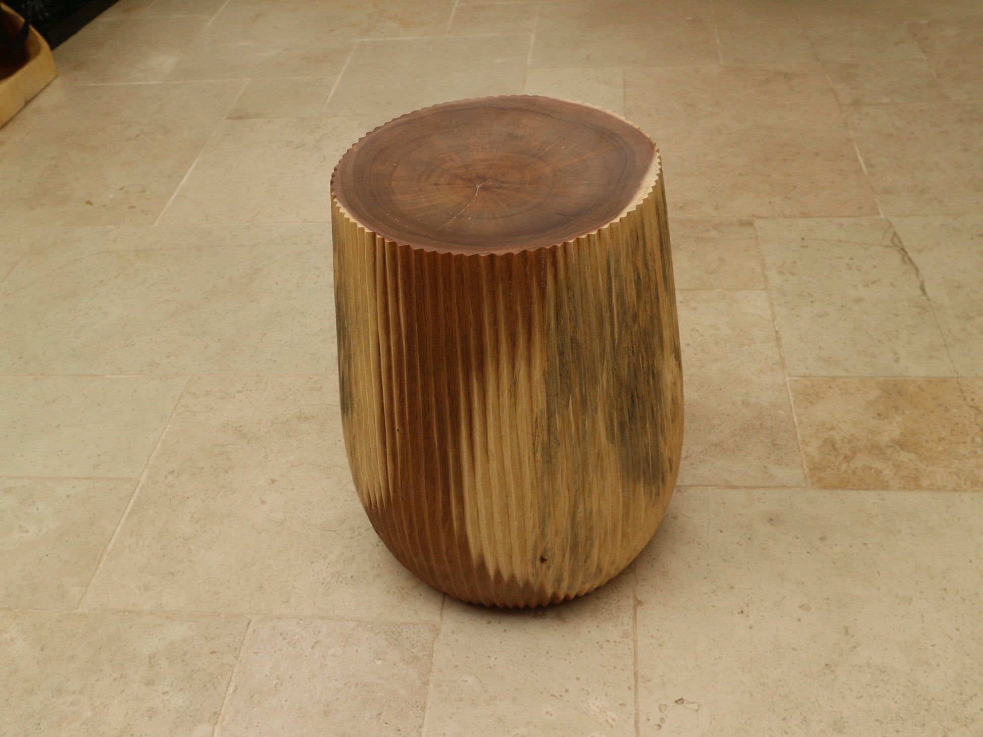 Alur Stool front view on stone floor showing rounded grooved teak form