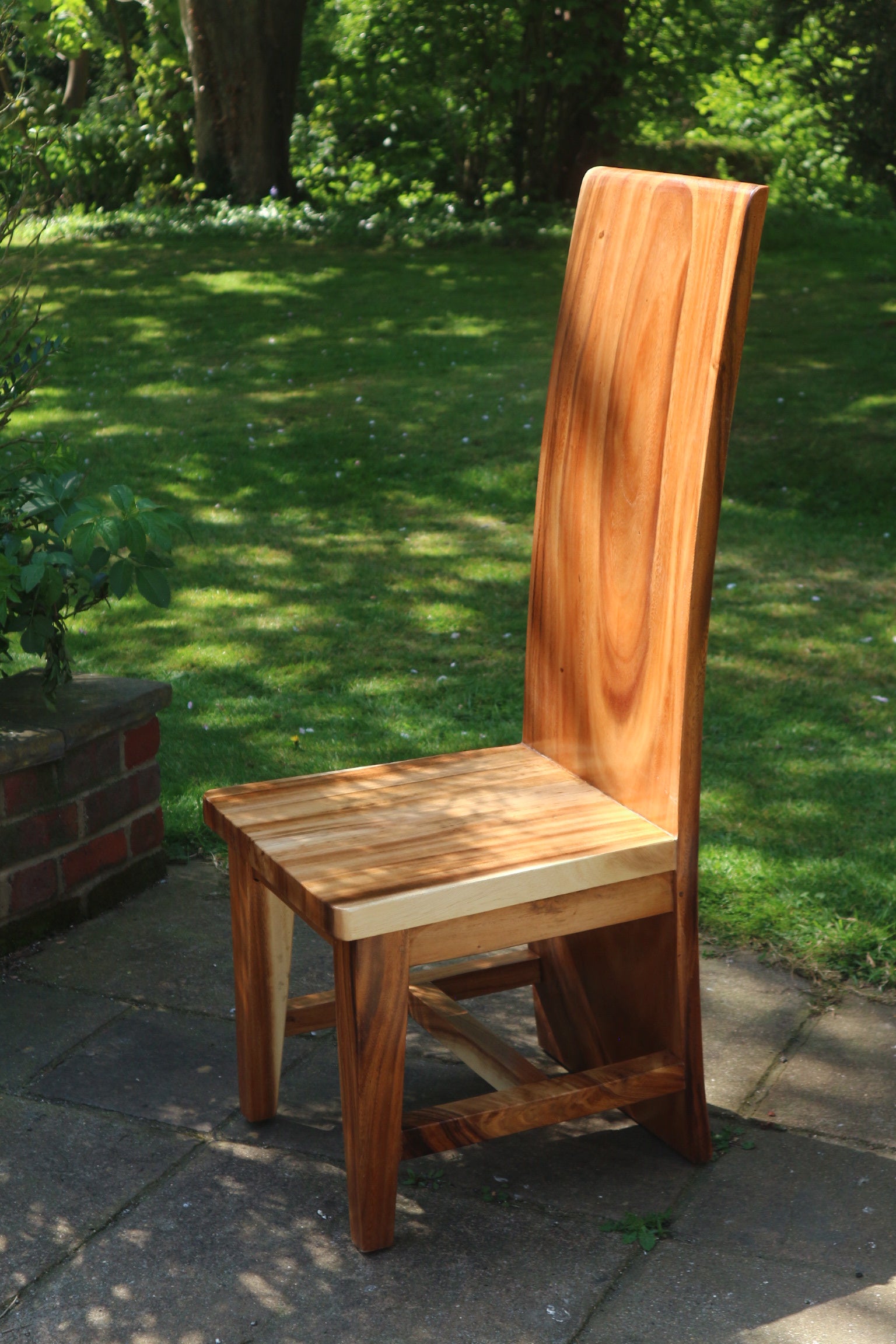 Angled view of the Monolit Chair revealing bold silhouette and rich teak grain