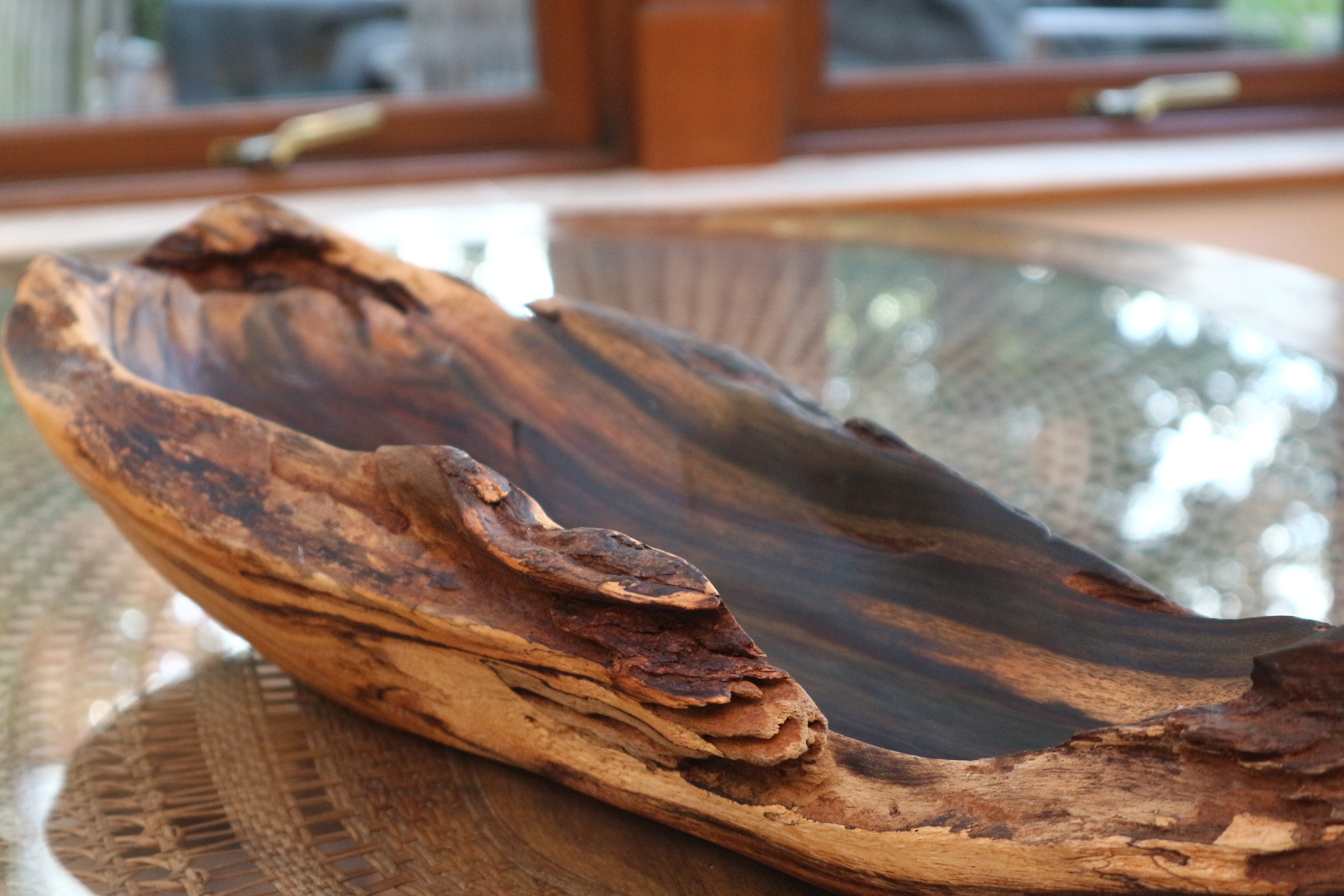 Wooden bowl with a natural, rustic finish on a glass table.
